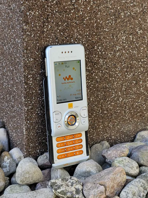 A white Sony Ericsson W580i, slid open, propped against stones