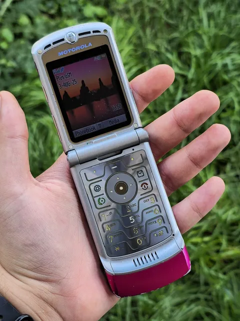 A pink Motorola RAZR V3, open, held in a hand